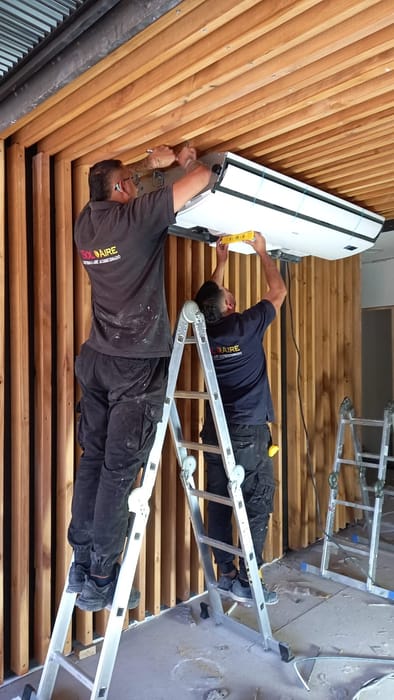Técnicos de Soloaire instalando la unidad interior de un aire acondicionado bajo un alero de madera