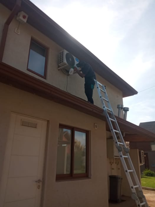 Técnico en escalera instalando una unidad exterior en el segundo piso de una casa