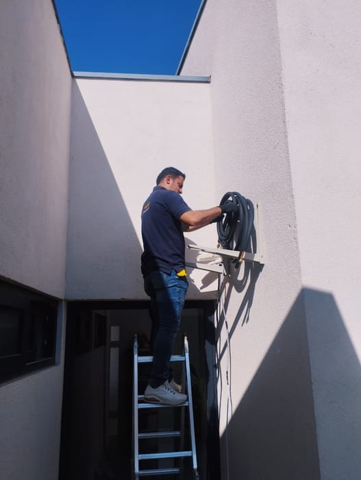 Técnico en escalera instalando una unidad exterior en un patio de luz