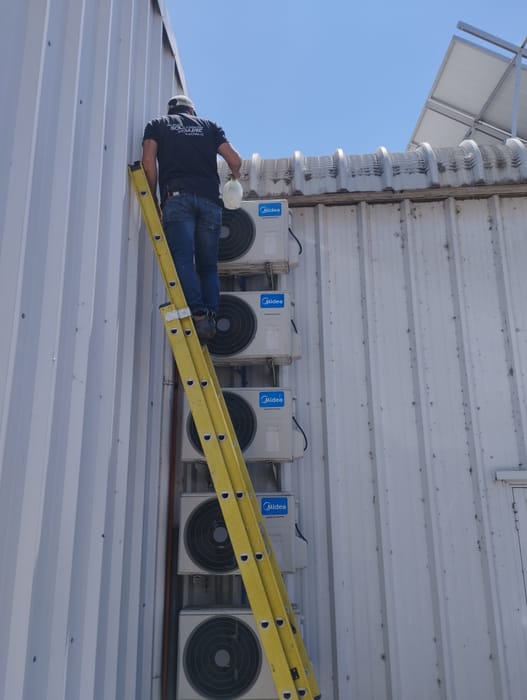 Técnico en escalera junto a una batería de unidades exteriores en una instalación industrial