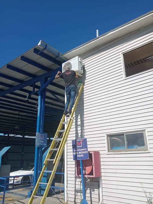 Técnico en escalera instalando aire acondicionado en un galpón industrial